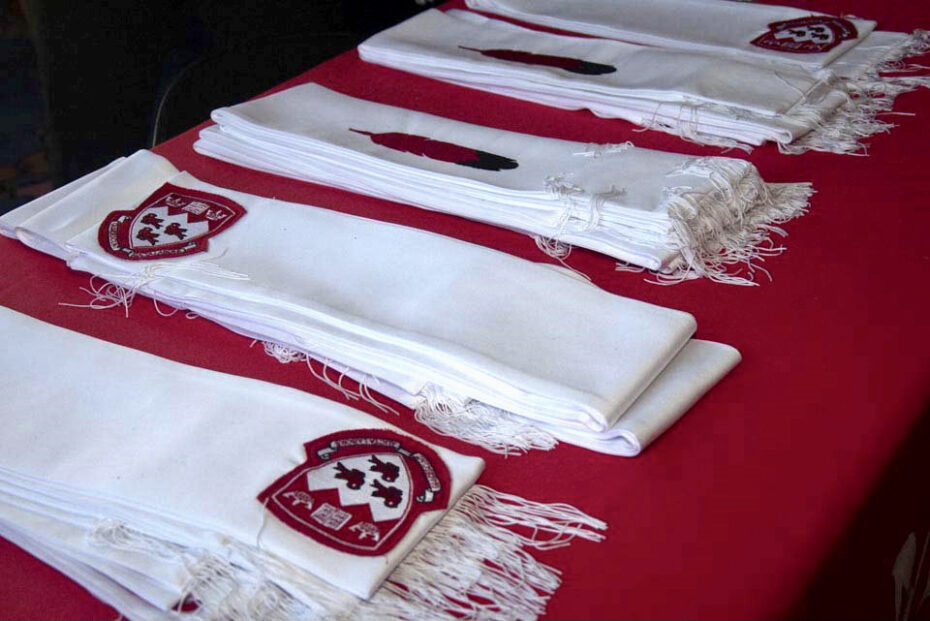 White scarves, bearing the McGill coat of arms and an eagle feather design, folded neatly on a red tablecloth