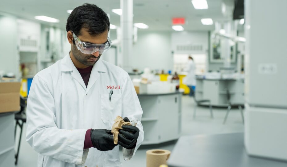 A McGill student with a white coat and protective glasses working in a chemistry lab.