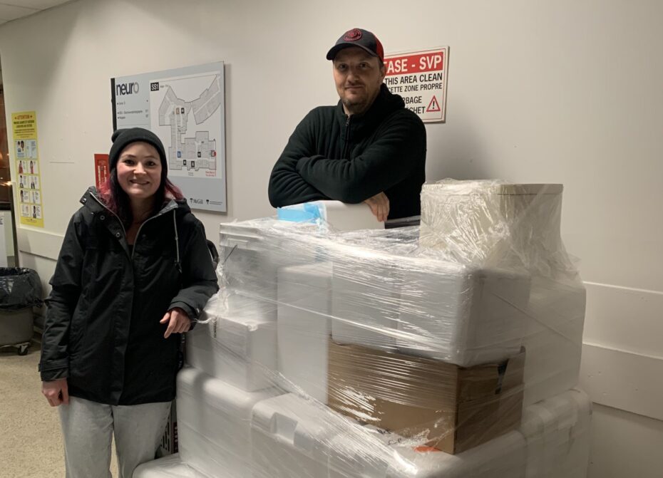Two Neuro lab members stand next to a pallet of Styrofoam containers and ice packs destined for Moisson Montreal, a local non-profit.