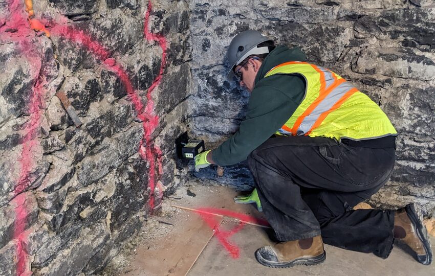 A person in a hardhat inserting a small machine into a brick wall.