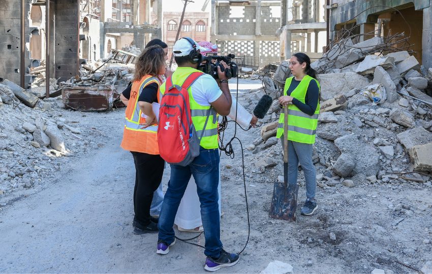 A new crew conducts a video interview in front of city debris and rubble. 