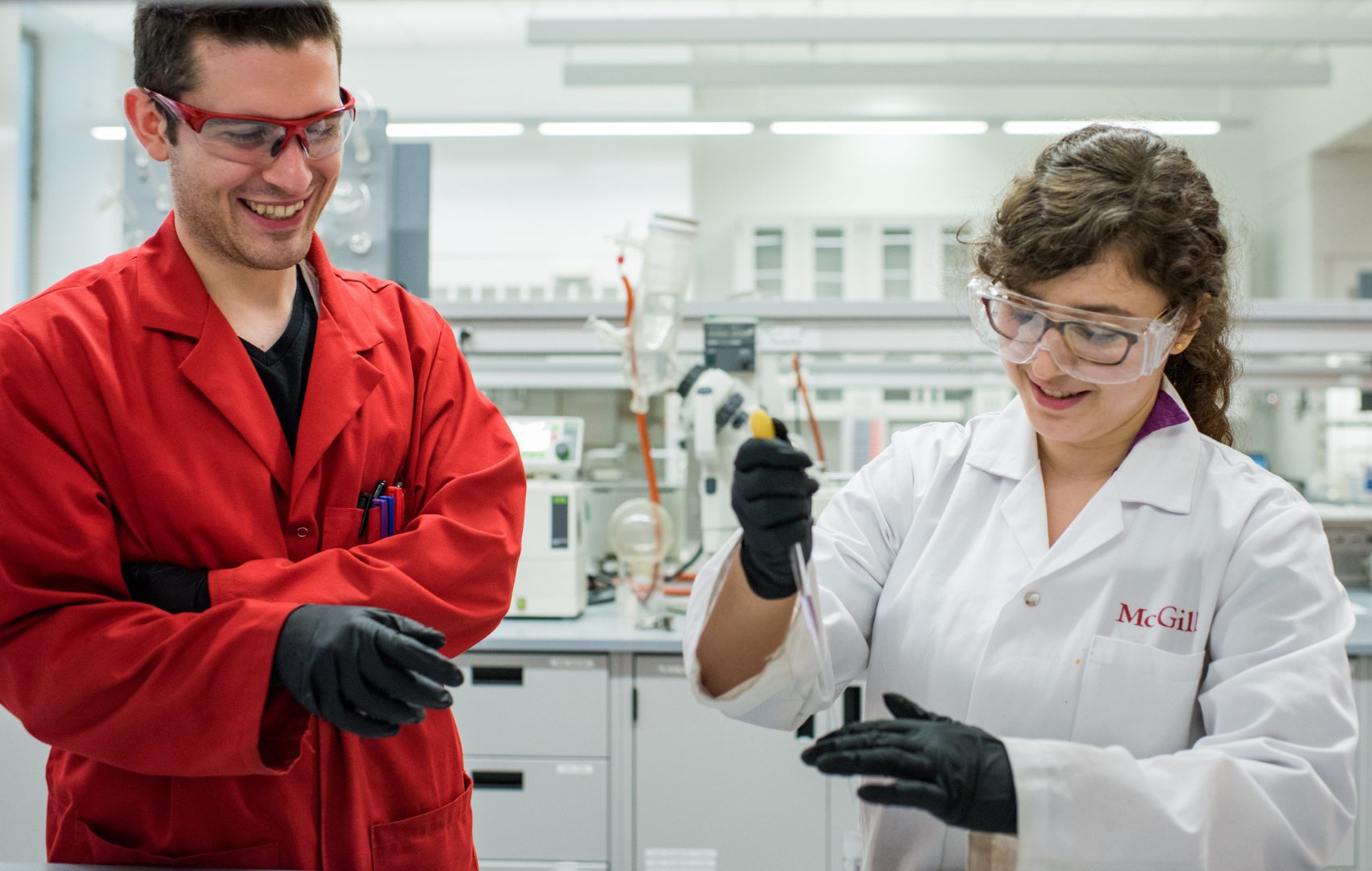 Deux étudiants souriants portant des blouses de laboratoire de McGill travaillent dans un laboratoire.