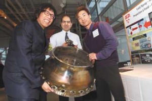 Professor Stephen Yue, Chair, Department of Mining and Materials Engineering (left), Ahmad Rezaeian, Postdoctoral fellow, Mining and Materials Engineering  (centre) and Wilson Wong, Master candidate, Mining and Materials Engineering (right), with part of a jet engine’s combustion chamber from their display for the research project Cold spray – hot stuff in aerospace materials engineering. / Photo: Owen Egan