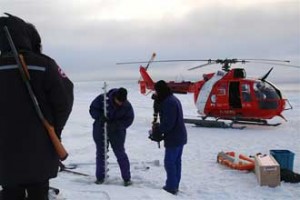 Researcher Bruno Tremblay prepares an auger to drill into an ice floe to insert a sonar to measure ice growth and melt. In the foreground, the helicopter pilot carries a gun to ward off polar bears. Photo courtesy of Bruno Tremblay